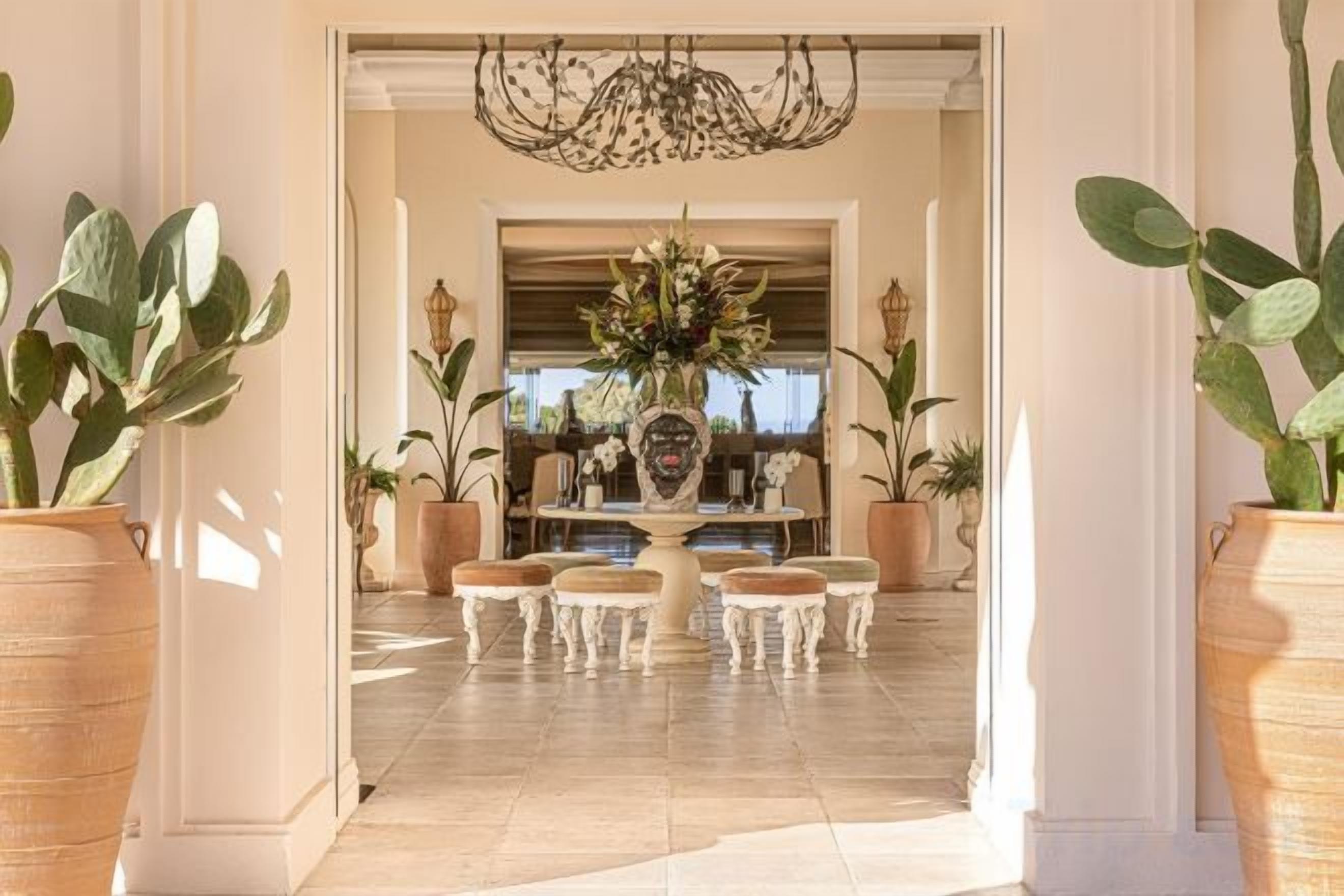 A grand entrance with a chandelier, a central floral arrangement, and potted plants.
