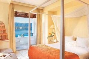 A hotel room with a bed, a balcony with a view of the sea, and a small table with a lamp. - Grecotel Eva Palace (Limni)
