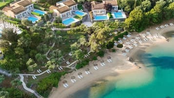 Vista aérea de un complejo turístico con varias edificaciones, una playa y una zona de piscina.