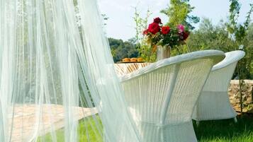 A wicker chair with a white canopy, a vase with red flowers, and a stone wall in the background.