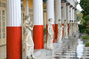 A row of statues on a tiled walkway with columns. - Grecotel Eva Palace (Limni)