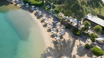 An aerial view of a beachside hotel with sun loungers and umbrellas, a clear pool, and lush greenery.