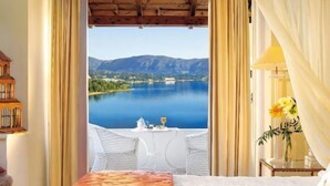 A bedroom with a bed, a table with a vase, and a view of a lake and mountains. - Grecotel Eva Palace (Limni)