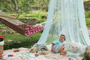A person relaxing on a hammock with a canopy, surrounded by a picnic setup with blankets and food items.