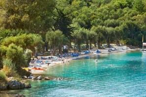 A beach with trees, a clear blue sea, and boats. - Grecotel Eva Palace (Limni)