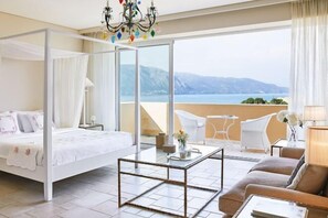 A bedroom with a four-poster bed, a glass coffee table, a sofa, and a balcony with a view of the sea and mountains. - Grecotel Eva Palace (Limni)