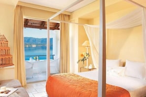 A bedroom with a four-poster bed, a balcony with a table and chairs, and a view of the sea. - Grecotel Eva Palace (Limni)