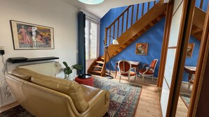 A living room with a sofa, a staircase, a dining area, and a painting on the wall. - Charming appartement with roof terrace in Vittel (Vittel)