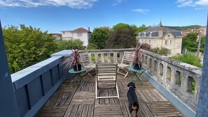 A rooftop terrace with a wooden deck, two folding chairs, a dog, and a view of surrounding buildings and trees. - Charming appartement with roof terrace in Vittel (Vittel)