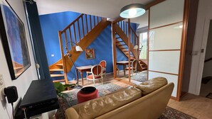 A room with a brown leather sofa, a wooden staircase, a dining table with chairs, and a large mirror. - Charming appartement with roof terrace in Vittel (Vittel)
