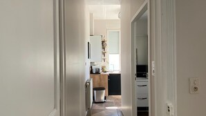 Un pasillo estrecho que conduce a una cocina con refrigerador, tostadora y una ventana con persianas.