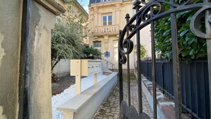 Una entrada con puerta de rejas y un camino de piedra que lleva a un edificio de fachada clásica y un reloj.
