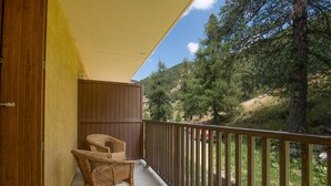 A balcony with wicker chairs, a wooden fence, and a view of a forested hillside.