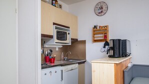 A compact kitchen with a microwave, sink, and small refrigerator. A wooden cabinet and a clock are also visible.