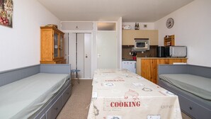 A compact room with two single beds, a kitchenette with a microwave, a small refrigerator, and a wooden cabinet.