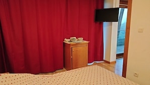 A bedroom with a bed, a wooden cabinet, a red curtain, and a television mounted on the wall. - Charming apartment on the ski slopes (Chamrousse)