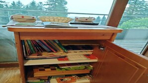 A wooden desk with a basket, a notebook, and a pen. Below the desk, there are shelves with books and a small toy. - Charming apartment on the ski slopes (Chamrousse)