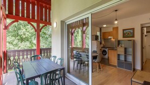 Un espace repas comprenant une table et des chaises, une porte-fenêtre coulissante donnant sur une cuisine, et une pergola rouge.