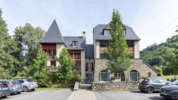 Un immeuble à plusieurs étages, doté d’une façade en pierre, d’une tour et d’un balcon. Des voitures sont garées devant.