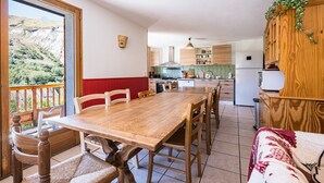 Un comedor con una mesa y sillas de madera, una cocina al fondo, y vistas a un paisaje montañoso a través de un ventanal amplio.