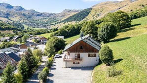 Un pueblo rural con un edificio blanco destacado y un balcón de madera, rodeado de vegetación exuberante y montañas al fondo.
