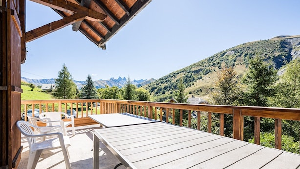 Una terraza de madera con una mesa y sillas, con vistas a un paisaje montañoso.