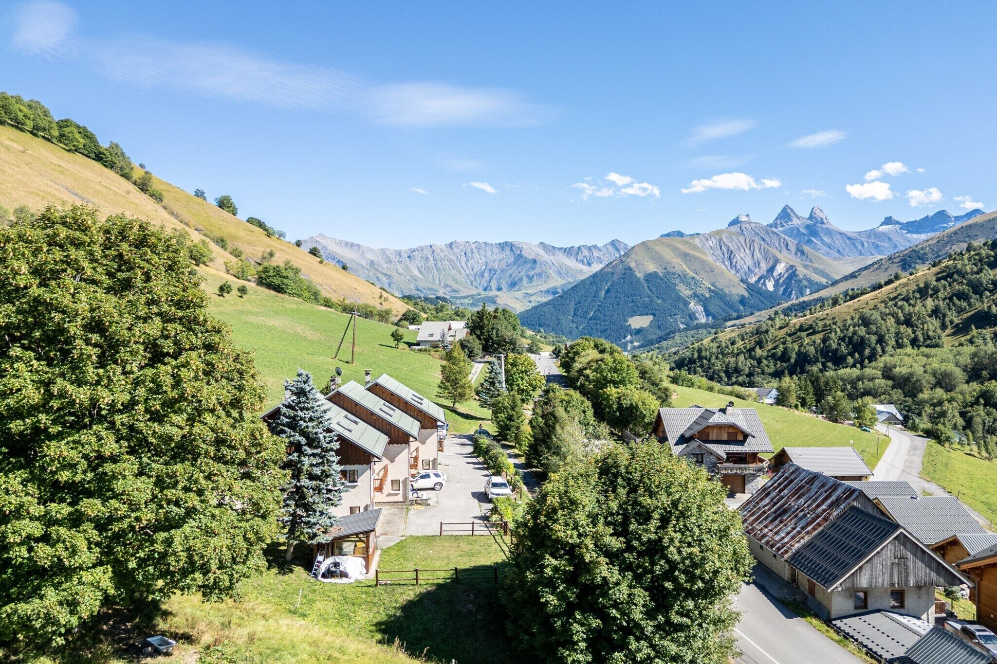 A mountain village with traditional wooden houses, a paved road, and a view of the surrounding mountains.