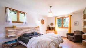 Un dormitorio con cama, mesita de noche, silla y ventana con cortinas.