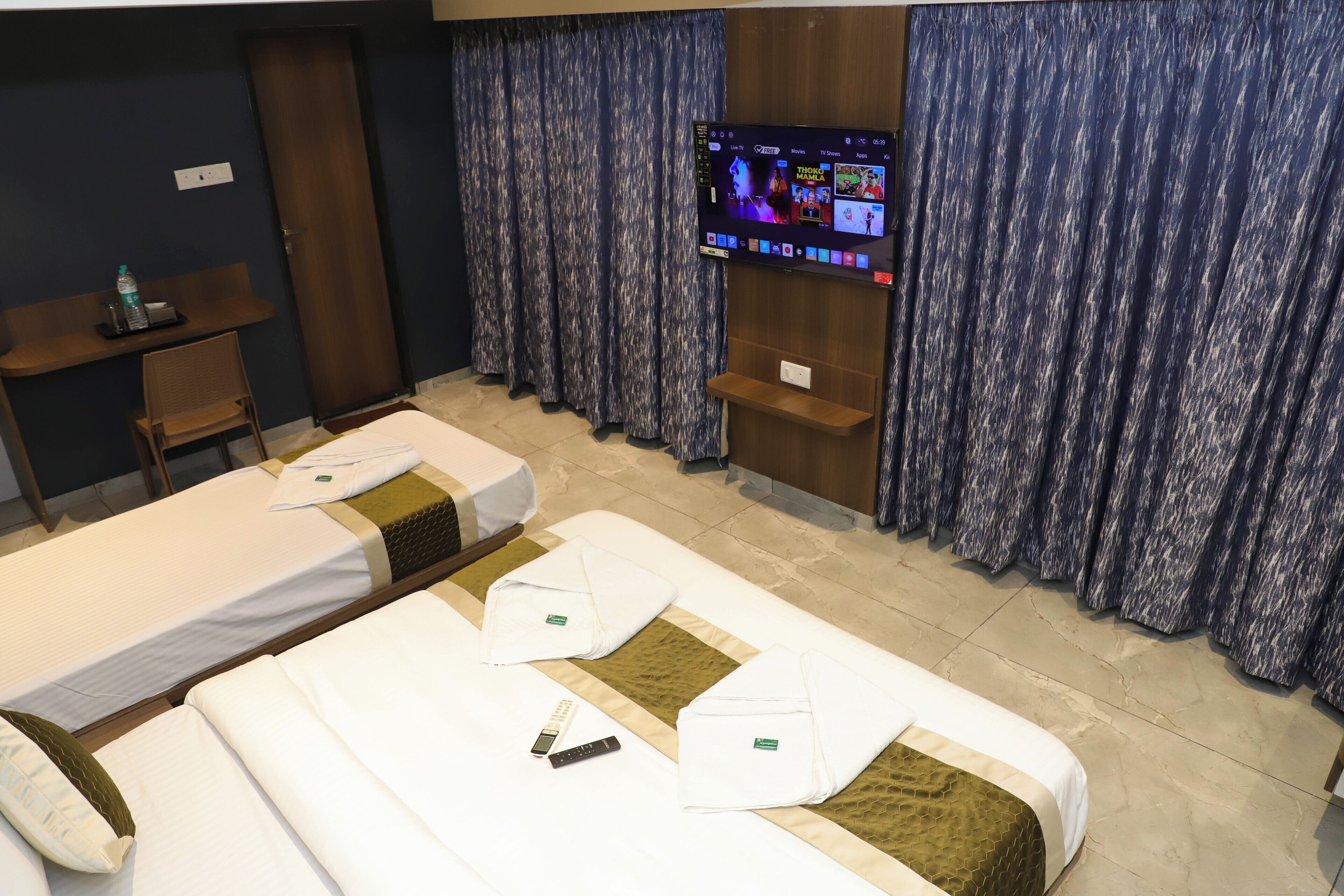 Ein Hotelzimmer mit zwei Betten, einem an der Wand befestigten Fernseher und einem Schreibtisch mit Stuhl.