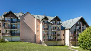 Ein mehrgeschossiges Wohngebäude mit Balkonen, einer flachen Dachterrasse und einem begrünten Innenhof.