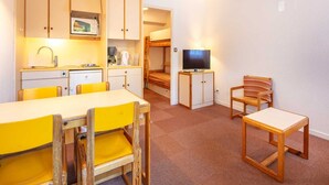 Ein gemütlicher Raum mit einer Küchenzeile, einem Esstisch mit gelben Stühlen, einem Fernseher auf einem Schrank und einem Hochbett im Hintergrund.