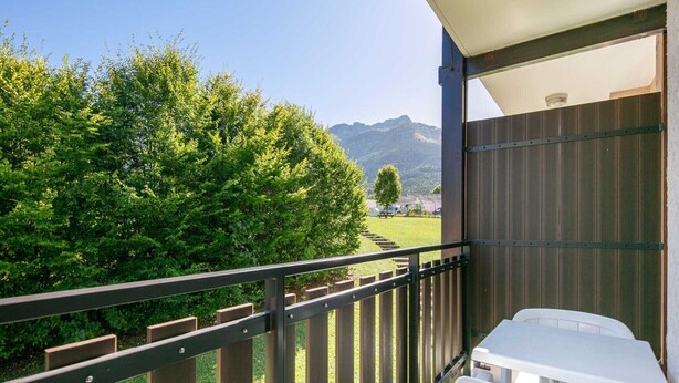 Ein Balkon mit Blick auf ein Gebirge, einem Holzzaun und einem weißen Tisch.