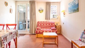 A cozy living room with a red patterned sofa, a wooden coffee table, and a dining table with chairs. A window with curtains is visible, and a painting hangs on the wall. - Mountain hideaway in Villard de Lans (Villard-de-Lans)