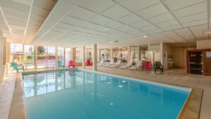 Una piscina interior con paredes de vidrio transparente, sillones de descanso y techo de azulejos.