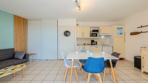 Un espacio habitable moderno y luminoso con un sofá, una mesa de comedor con sillas, una zona de cocina y una pequeña mesita auxiliar.