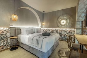 A modern bedroom with a large bed, a side table, a chair, and a dining area. - Wyndham Grand Crete Mirabello Bay (Agios Nikolaos)