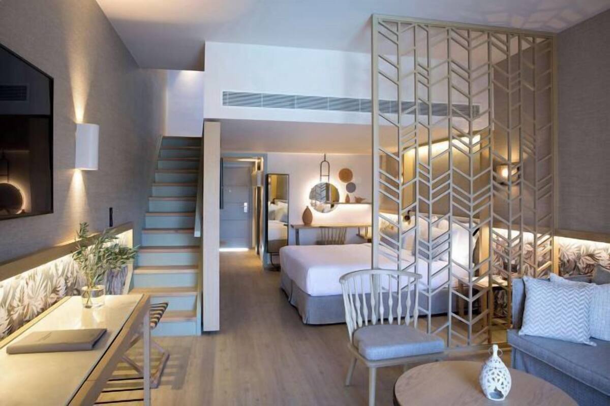 A modern hotel room with a staircase, a bed, a sofa, and a dining area.