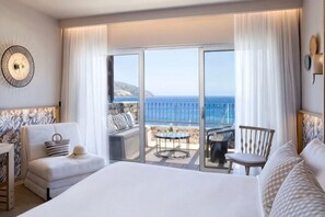 Une chambre d’hôtel dotée d’un grand lit, d’un coin salon avec une table et d’un balcon offrant une vue sur la mer.