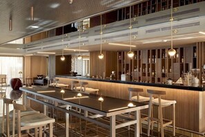 A modern bar area with a long counter, multiple hanging lights, and bar stools.