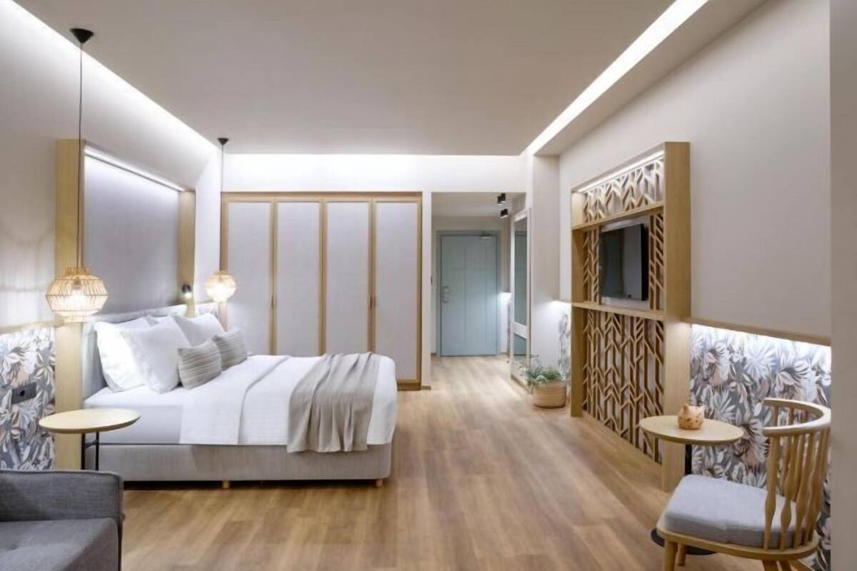 A modern hotel room with a bed, bedside tables, a TV, and a seating area.
