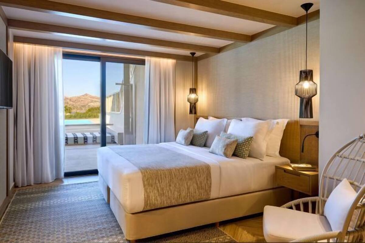 A hotel room with a large bed, a chair, a TV, and a view of the outdoors.