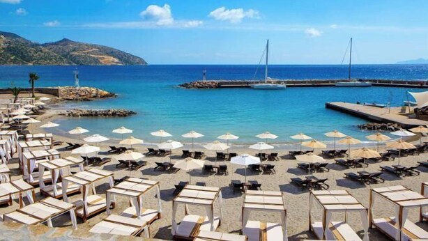 Une plage bordée de rangées de chaises longues et de parasols, une jetée et un phare en arrière-plan.