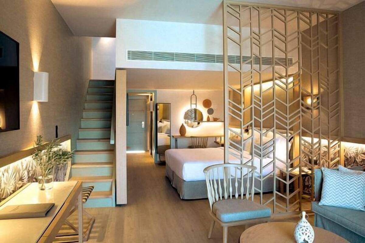 A modern hotel room with a staircase, a bed, a desk, and a seating area.