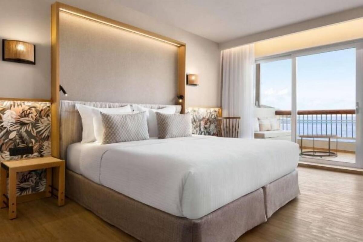 A large bed with a headboard, a bedside table, and a view of the ocean through a balcony.