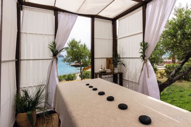 A massage table with black stones, a view of a pool, and a covered outdoor area with curtains.