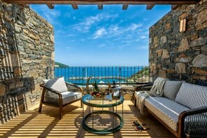 A stone-walled outdoor seating area with a pool, a glass table, and a sofa. - Wyndham Grand Crete Mirabello Bay (Agios Nikolaos)