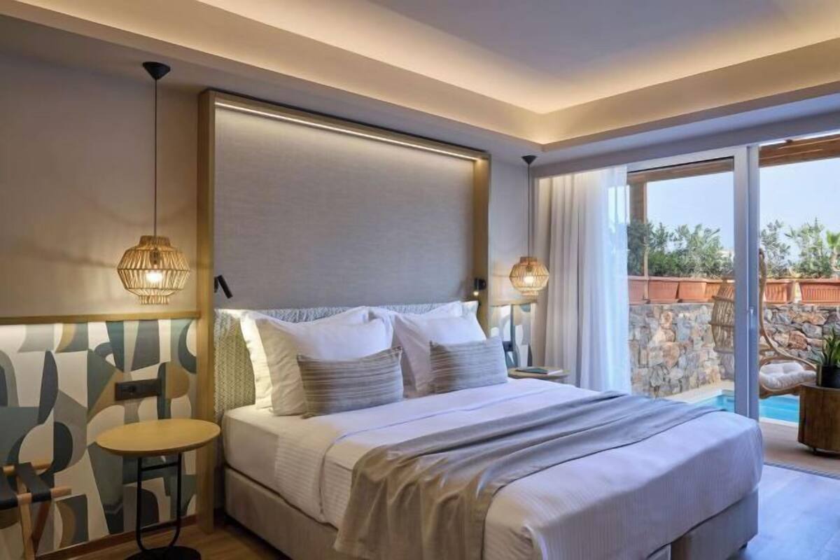 A bedroom with a bed, bedside tables, a chair, and a view of an outdoor area with a pool.