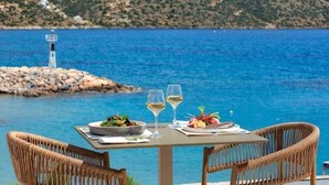Une table dressée avec un repas et des verres, donnant sur une étendue d’eau et une île rocheuse.