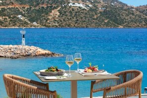 Une table dressée avec un repas et des verres, donnant sur une étendue d’eau et une île rocheuse.