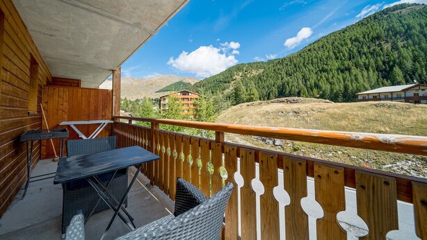 A wooden balcony with wicker furniture and a view of a mountainous landscape. - Family-friendly apartment with terrace (Allos)